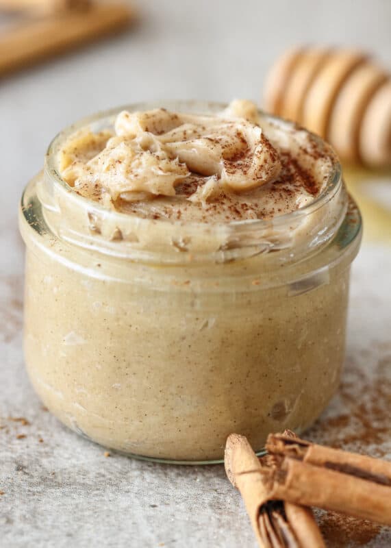 A glass jar of Pumpkin Spice body butter with 2 cinnamon sticks in the lower right corner. 