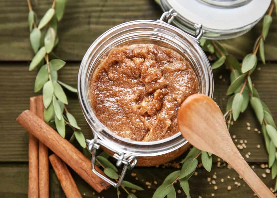 A closeup image of the DIY apple sugar scrub in a glass jar with a wooden spoon propped on the edge. 